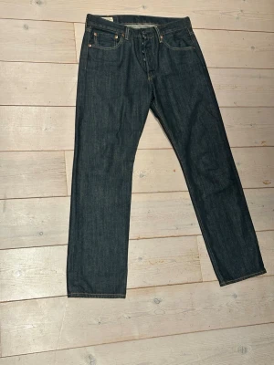 Levi's 501 mörkblå raka jeans - Klassiska Levi's 501 jeans i mörkblå denim med raka ben och femficksmodell. Jeansen har knappgylf, kontrastsömmar och den ikoniska läderpatchen bak i midjan. Perfekta för en clean och tidlös look. Använda 2 gånger. Priset kan diskuteras.