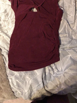 Vinröd body med cut out och smala band - Säljer en vinröd body med smala axelband och snygg cut out-detalj framtill. Bodyn har en åtsittande passform och är tillverkad i ett stretchigt, mjukt material som känns bekvämt mot huden. Perfekt att styla med jeans eller kjol för en trendig look.