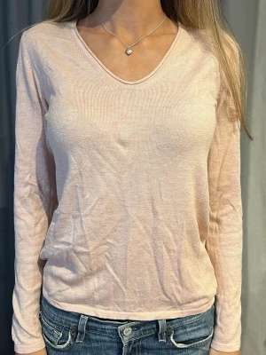 Ljusrosa långärmad topp med v-ringning - En enkel och stilren ljusrosa långärmad topp med v-ringning. Tillverkad i ett mjukt och tunt material som känns skönt mot huden. Perfekt att matcha med jeans eller kjol för en avslappnad look.