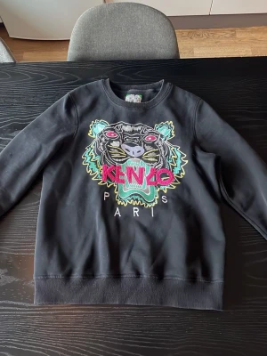 Svart Kenzo sweatshirt med tiger - Säljer min kenzo tröja som är UNISEX, säljer för ja aldrig använder den längre. Den passar storleken ungefär 160-170 skulle jag säga. Inga skador eller liknande på den!