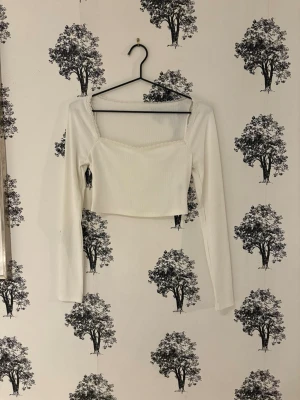 Vit croppad långärmad topp - Trendig vit croppad topp med lång ärm och fyrkantig urringning. Tillverkad i ribbad bomull som ger en skön och stretchig känsla. Perfekt att styla med höga jeans eller kjol för en clean look.