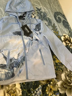 Ljusblå vindjacka med örntryck från Trapstar - Säljer Trapstar vindjacka helt nytt använd bara 3  gånger säljs pågrund ej behov av den längre köpt ny 