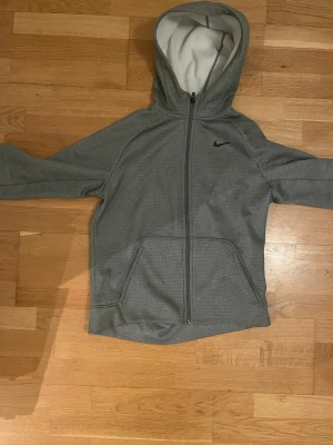 Grå Nike Therma-Fit hoodie XL - Säljer en grå zip-hoodie från Nike i modellen Therma-Fit. Hoodien har dragkedja framtill, två stora fickor och en mjuk, vit fleece på insidan. Klassisk Nike-logga på bröstet och huva för extra komfort. Perfekt för chill eller träning. Storlek 158-170 pris kan Diskuteras!