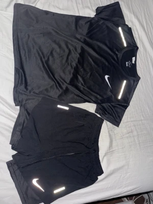 Svart träningsset från Nike - Säljer ett svart träningsset från Nike med t-shirt och shorts. Båda plaggen har vita reflexdetaljer och Nike-logga. Materialet är lätt och andas, perfekt för löpning eller gym. Storlek S men små i storlek. Kan ge billigare på snabb affär. Oanvända.