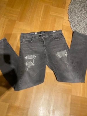 Grå slitna jeans med raka ben - Snygga grå jeans med slitningar och hål på båda ben. Jeansen är från replay. Storlek W32 L34. Kan gå ner i pris vid snabb affär.
