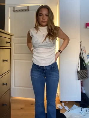 Vit ribbad ärmlös polotopp - Snygg vit ärmlös polotopp i ribbat material. Toppen har en hög hals och sitter tajt mot kroppen, perfekt att styla med både jeans och kjol. Enkel och stilren design som passar till många olika looks.