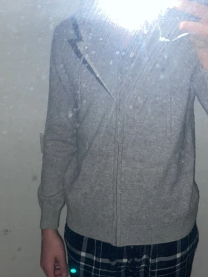 Grå zip-hoodie med huva - En enkel och stilren kashmir  grå zip-hoodie med dragkedja framtill och huva med snören. Tröjan har långa ärmar och ribbade muddar vid ärmslut och nederkant. Perfekt för en avslappnad look och passar till det mesta.