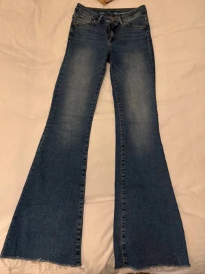 Jeans - Säljer ett par blå bootcut jeans med rå, fransig kant nedtill. Jeansen har klassisk femficksdesign och en snygg tvätt med ljusare partier framtill. 