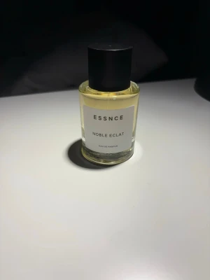 ESSNCE Noble Eclat Eau de Parfum - ESSNCE Noble Eclat Eau de Parfum kommer i en stilren, genomskinlig glasflaska med svart lock. Doften har inslag av vanilj, kanel och torkad frukt, vilket ger en varm och kryddig karaktär. Perfekt för dig som gillar unika och sofistikerade parfymer. (ALL INFO om parfymen finns på hemsidan!)