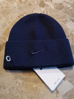 Nike mössa ny - Fin nike mössa som original märket är Nike.. Den är helt oanvänd med alla etiketter på. Alla qr koder elder till deras hemsida så att den är riktig. Mössa är fin och stretchig om tillåter dig att ha en stor komfort. Skriv till mig om det är frågor!