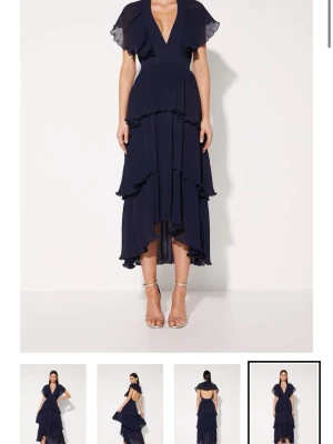 Mörkblå omlottklänning med volang - Snygg mörkblå festklänning med djup v-ringning och volangdetaljer. Ifrån mossman. Använd 2 gånger. Klänningen har korta ärmar och är tillverkad i ett lätt, plisserat material som ger en luftig känsla. Perfekt för dig som gillar en feminin och trendig stil.