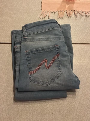 Ljusblå jeans med broderad bakficka - Snygga ljusblå jeans från Nelly (only)med en unik broderad detalj i rött och vitt på bakfickan. Jeansen har klassisk femficksdesign, dubbla knappar i midjan och smal passform. Perfekta för dig som gillar en stilren men ändå personlig look.