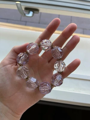 Armband med stora ljus lila glaspärlor med guldiga detaljer - Säljer ett jätte fint armband med stora, facettslipade lila glaspärlor och små guldfärgade detaljer mellan pärlorna. Armbandet har en elastisk tråd som gör det enkelt att ta på och av. Perfekt för dig som gillar statement-smycken och vill ha något som verkligen syns.