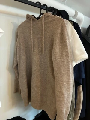 Merinoull hoodie - Mysig beige hoodie med huva och dragsko. Tillverkad i mjukt stickat material som känns skönt mot huden. Perfekt för en avslappnad och stilren look. Personen på bilden är 183 hör av er vid frågor.