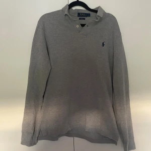 Grå pikétröja Polo Ralph Lauren M - Klassisk grå pikétröja från Polo Ralph Lauren i storlek Medium. Perfekt för en clean och stilren look. Väldigt fint skick.