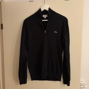 Lacoste half zip tröja - En half zip tröja från Lacoste i mörk grå färg, dessutom är skicket väldigt bra. Vid frågor, hör av er!