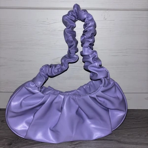 Lila axelväska  - • Lila handväska  • Använd ett fåtal gånger  • Metallknapp som öppnar och stänger väskan