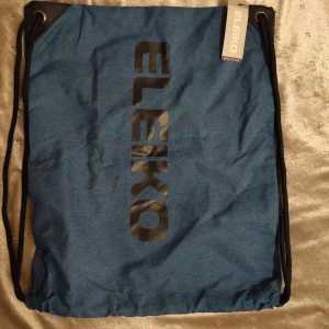 Gym påse - Snygg blå gympåse från Eleiko med svart logga framtill. Väskan har svarta snören och är tillverkad i slitstark polyester, perfekt för att bära träningskläder eller skor. Enkel och stilren design som passar dig som gillar sportiga accessoarer.
