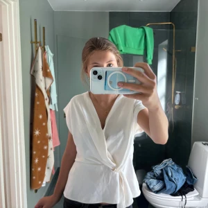 Vit omlottopp med knyt i midjan - Snygg vit omlottopp med knyt i midjan och v-ringad hals. Toppen har korta ärmar och ett luftigt, flowy tyg som ger en avslappnad men stilren look. Perfekt att matcha med jeans eller kjol för en fräsch vibe. Bara använd max 2 gånger den har blivit tvättad en gång🫶🏻🫶🏻🫶🏻