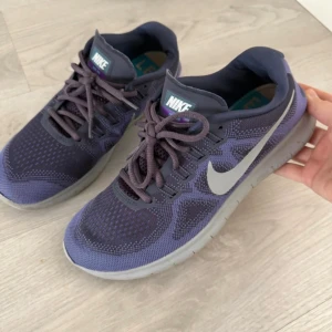 Nike Free 5.0 lila sneakers - Nike Free 5.0 sneakers i mörklila med grå sula och silverfärgad swoosh. Ovandelen är i ventilerande syntetmaterial med stickad mesh och snörning. Rund tå och platt sula för skön komfort. Perfekt för dig som gillar sportig stil och vill ha lätta skor.