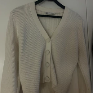 Vit/Beige ribbad kofta från Zara - Säljer en beige ribbad kofta från Zara med v-ringning och stora tygklädda knappar framtill. Koftan har lång ärm och är gjord i ett mjukt stickat material som är perfekt för lager-på-lager. Enkel och stilren design som passar till allt. Inhandlades för 399 kr - säljer för billigare!♥️