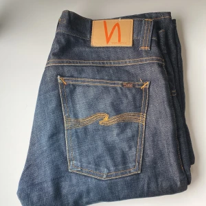 Nudie Jeans sven blå 32/34 - Snygga blå jeans från Nudie Jeans med klassisk femficksdesign och orangea sömmar. Modellen har rak passform och är tillverkad i 100% bomull. Bakfickan har Nudies ikoniska broderi och läderpatch med logga. Perfekt för dig som gillar stilrena jeans.kom med bud!!!!