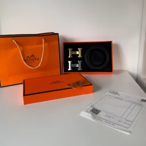 Svart H bälte med H-spänne - Säljer ett svart H bälte i skinn med två utbytbara H-spännen i guld och silver. Bältet är stilrent och klassiskt, levereras i original orange box med tillhörande påse och kvitto. Perfekt accessoar för att lyfta din outfit.