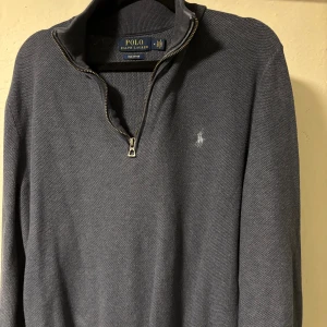 Blå half zip tröja Polo Ralph Lauren - Snygg mörkgrå tröja från Polo Ralph Lauren med half zip och klassisk krage. Tröjan har lång ärm och är tillverkad i mjuk bomull. Diskret logga broderad på bröstet. Perfekt för dig som gillar stilrena och tidlösa plagg.