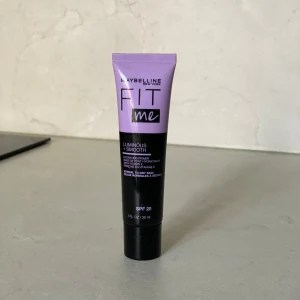 Maybelline Fit Me Luminous + Smooth Primer - Hydrerande primer från Maybelline Fit Me med SPF 20, perfekt för normal till torr hud. Tuben är lila och svart, innehåller 30 ml och är berikad med vitamin E för en fin och jämn bas.