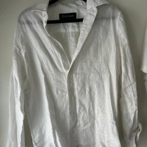 Vit linneskjorta från ST Studios XS - Fräsch vit skjorta från TS Studios i storlek XS, tillverkad i svalt linne. Klassisk krage, långärmad och med knappar framtill. Perfekt för dig som gillar en clean och enkel stil. Skjortan har en loose passform och är riktigt skön att bära under varmare dagar.