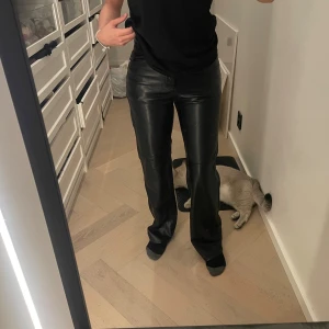 Svarta skinnbyxor från Bershka - Säljer ett par svarta skinnbyxor från Bershka i storlek XS. Byxorna har raka ben, klassisk femficksmodell och hög midja. Snyggt glansigt material som ger en edgy vibe och passar perfekt till en cool streetstyle-look.