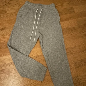 Grå mjukisbyxor med snörning - Snygga grå mjukisbyxor från H&M med vita snören i midjan och resår. Byxorna är långa och har en avslappnad passform och resår vid anklarna. Byxorna har stora fickor i sidorna. Mjukisbyxorna är i väldigt fint skick o endast använda en gång. Ytterst liten fläck på ena snöret som inte är märkbar. Skriv privat för fler bilder. 