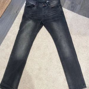 Svarta jeansbyxor från H&M Denim - Snygga svarta jeansbyxor från H&M Denim med lätt tvättad look och klassisk femficksdesign. Jeansen har normal passform och raka ben, tillverkade i bomullsmaterial. Perfekta för dig som gillar en stilren och enkel vibe. Storlek: 32/32