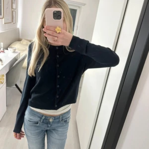 Mörkblå kofta  - Säljer en mörkblå, croppad med rund halsringning och knappar framtill. Koftan har långa ärmar och är i mjuk bomullsblandning, perfekt att slänga över ett linne eller t-shirt. Enkel och stilren modell som funkar till jeans eller kjol.