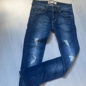 Levi's 511 blå skinny jeans herr  - Säljer ett par Levi's 511 skinny jeans i mörkblå tvätt med slitna detaljer och lagningar på benen. Klassisk femficksmodell med låg till normal midja och smal passform hela vägen ner. Perfekta för dig som gillar en modern och avslappnad stil. Priset kan ändras