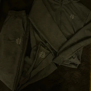 Grå mjukisbyxor med broderad logga - Grå mjukisbyxor med resår i midjan och broderad vit logga på benet. Byxorna är i mjukt material och har en avslappnad passform, perfekta för chill dagar. Matchar med hoodie i samma stil.