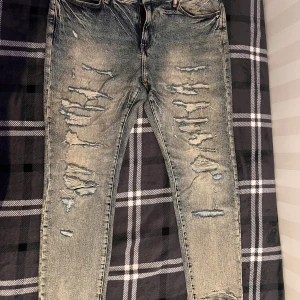 Rippade skinny jeans från H&M - Säljer ett par blå skinny jeans från H&M med slitna och rippade detaljer framtill. Jeansen har klassisk femficksdesign, normal midja och är tillverkade i stretchig denim för en tight passform. Perfekta för dig som gillar en edgy streetstil.