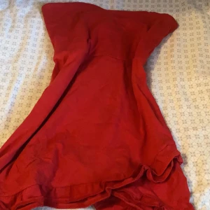 Röd kortklänning med volang - Säljer en snygg röd kortklänning med volangdetaljer i nederkant. Klänningen har en enkel och stilren design med en mjuk och lätt känsla, perfekt för dig som gillar färgstarka plagg. Passar dig som vill sticka ut med en klassisk röd look.