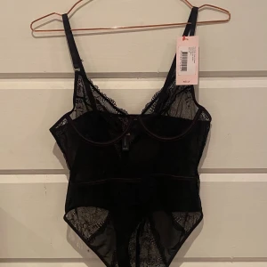 svart body Nelly - Supersnygg svart korsettbody från Nelly. Gjord i transparent spets med tunna axelband och bygel under bysten. Utskurna detaljer framtill och vackra spetsmönster ger en extra touch. Perfekt för dig som vill ha något unikt och trendigt. Oanvänt på grund av fel storlek. Original priset är 219 på deras hemsida 