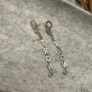 Silvriga örhängen med texten STRONG ifrån Ioaku - Unika silvriga örhängen med kvinnosymbol upptill och hängande bokstäver som bildar ordet STRONG. Ifrån Ioaku. Dom är knappt använda och kommer med box. 
