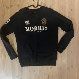 Mörkblå sweatshirt från Morris  - Säljer en mörkblå sweatshirt från Morris Gents med broderad logga, brittisk flagga och stort tryck på bröstet. Snygg detalj med siffran 8 på ena ärmen. Klassisk rund hals och långa ärmar. 