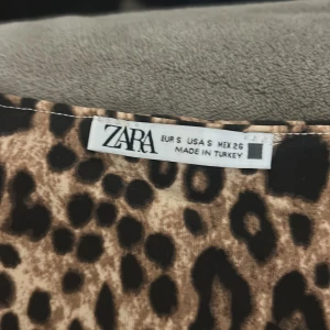 Leopardmönstrad klänning från Zara - Snygg kort klänning från Zara med leopardmönster i bruna och svarta toner. Ärmlös modell med figurnära passform och rund halsringning. Perfekt för dig som vill sticka ut med en djärv look.