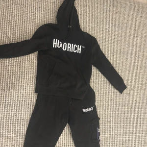 Svart hoodie från Hoodrich - Svart hoodie från Hoodrich med stor vit logga framtill och unikt tryck i vitt och lila på ryggen. Klassisk känguruficka, snörning i huvan och långa ärmar. Perfekt streetwear-vibe och riktigt skön passform. Använder inte den nå mer för att jag har tröttnat. Den har inga defekter och har inte använt så mycket men har haft den i snart 2 år. skriv privat så kan pris diskuteras.