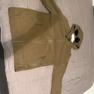 Beige hoodiejacka från C.P. Company M - Säljer en kofta från C.P. Company i storlek M. Jackan har dragkedja framtill, två snedställda fickor med dragkedja och den ikoniska huvan med inbyggda goggles. Perfekt för dig som vill sticka ut. Inga skador på den här använt den 2-3 gånger. Pris går att diskutera.