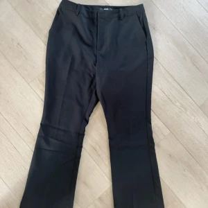 Svarta kostymbyxor från BikBok - Svarta kostymbyxor från BikBok i klassisk rak modell med pressveck och hällor för bälte. Byxorna har fickor i sidorna och två dekorativa bakfickor. Perfekta för en clean och stilren look.