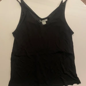 Svart linnetopp från H&M, storlek S - Svart linnetopp från H&M i storlek S. Toppen har smala axelband och en klassisk, enkel design med rundad halsringning. Materialet är mjukt och lätt, perfekt för varma dagar eller som layering-piece. Snygg att matcha med jeans eller kjol.