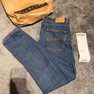 Nudie Jeans Lean Dean blå 32/32 - Säljer ett par Nudie Jeans lean dean i modellen Troubled Sea. Klassiska blå jeans med snygga kontrastsömmar i gult och ikonisk bakficka. Tillverkade i 99% bomull och 1% elastan för lite stretch. Perfekt passform och stilren look. Dom är köpt på NollNitti för 1599kr och kvitto finns på bilden längst bak 🧾 