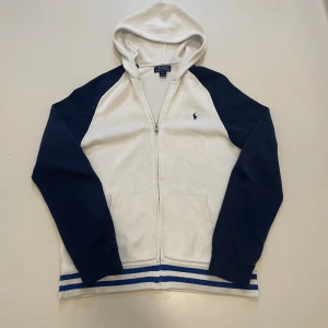  Stickad Ralph Lauren hoodie - Hej, jag säljer en vit och blå stickad hoodie från Ralph lauren. Jag säljer den eftersom den är lite för liten för mig. Det finns en liten fläck vid högra magficka som tyvär inte går bort men syns knappt. Hör av dig vid minsta fundering