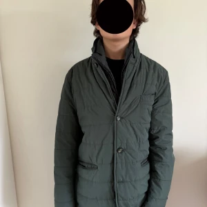 Snygg Grön kavajjacka - Snygg mörkgrön kavajjacka med klassisk krage, knappar framtill och två fickor med snygga detaljer. Jackan har en innerkrage och är perfekt för kyligare dagar. Stilren design med raka linjer och diskret bröstficka.