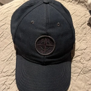 Mörkblå keps från Stone Island  - Snygg keps använd relativt mycket men ändå i väldigt bra skick. Står junior storlek 3 men passar även vuxen